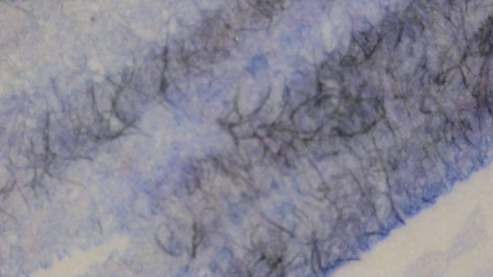 Photo of ink blob on paper under magnification. Paper fibers are visible. There are both blue and dark gray areas in the blob, with some paper fibers being very dark gray, and some lighter areas being almost completely light blue.