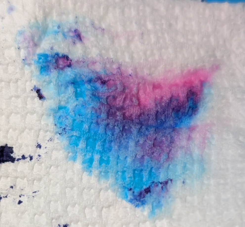 Photo of ink on a paper towel. Some splotches are purple, but there are distinct areas of light blue, dark blue, purple, and magenta