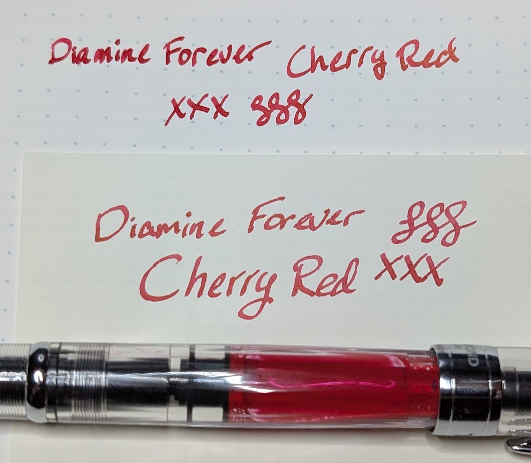 Photo of two writing samples and a fountain pen containing red ink. Taken from the top-down. Both samples say "Diamine Forever Cherry Red" followed by three "X"s and three curlicues. The ink is a bold red.