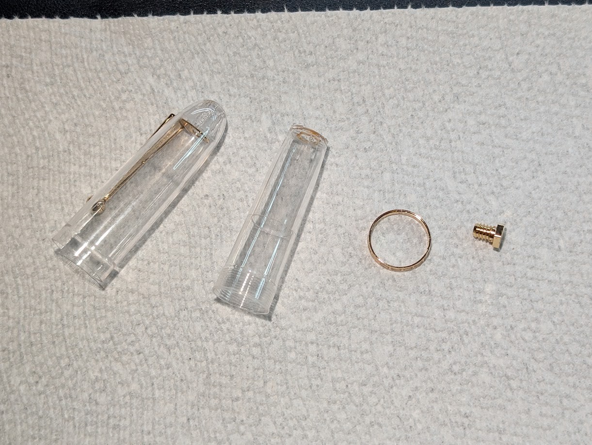Photo of several items spread out on a paper towel: - The Jinhao 9019 outer cap with the clip attached, clean. - The Jinhao 9019 inner cap, clean - The screw that holds the inner cap, outer cap, and clip together. It is only a few mm long and has a 7mm hex head on it. - Gold accent ring that goes around the inner cap