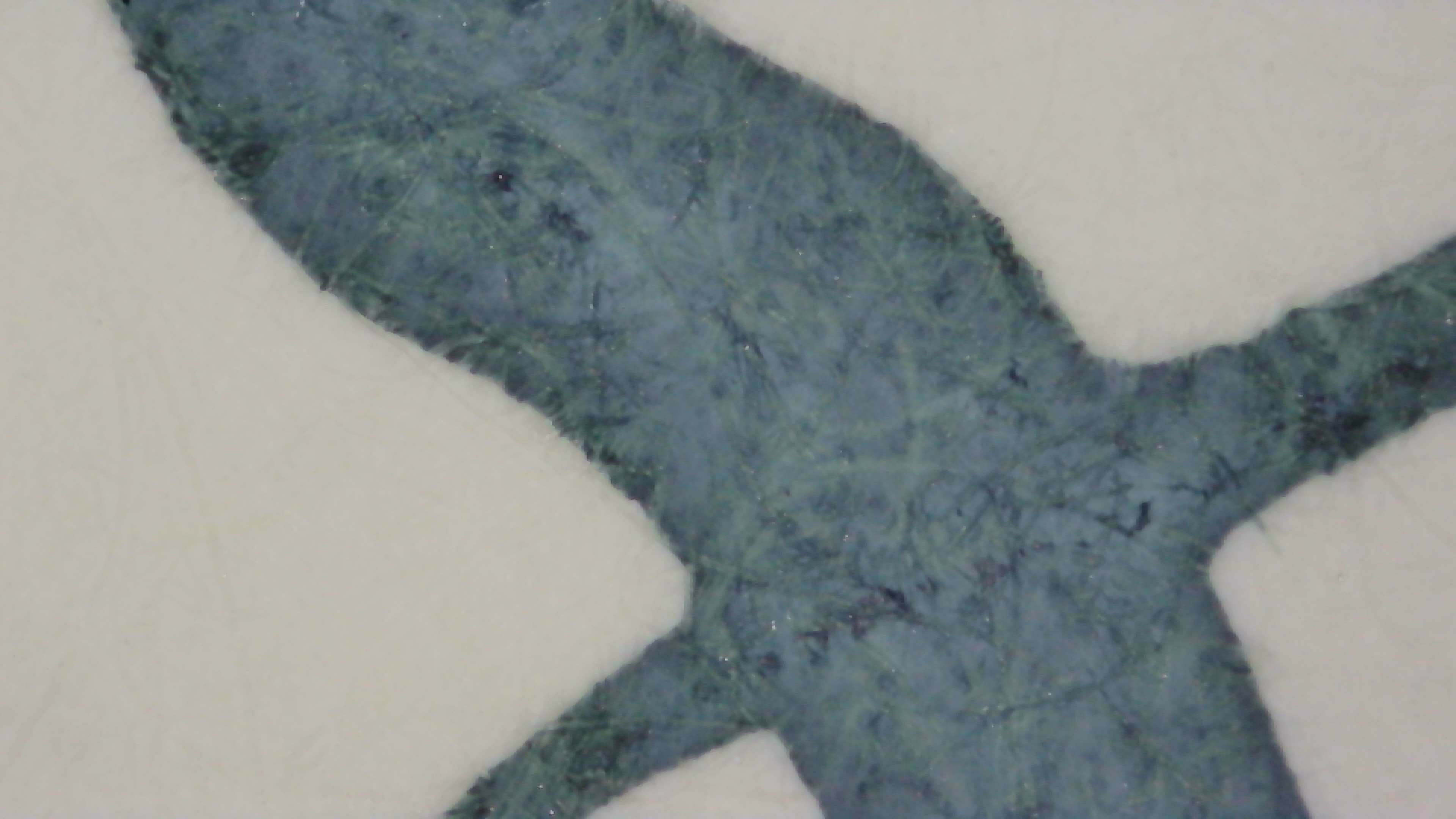 Photo of ink on paper under magnification. Most of the ink is a dark slate teal, but some paper fibers are green, some are dark blue, and around the edges both are darker.