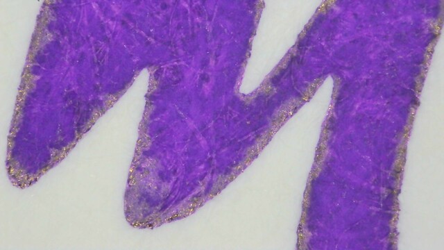 Photo of ink writing on Iroful paper under magnification. The ink is purple, with a couple places inside that are lighter on paper fibers. The edges of the lines are extremely smooth. There is a distinct visible near constant outline of gold sheen around the edges of the lines.
